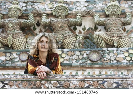 Attractive woman tourist with long hair on the background of the stone figures of the temple complex of Wat Arun Thailand smiles and looks