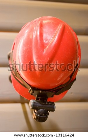 A red hard hat with a light hanging on the wall.