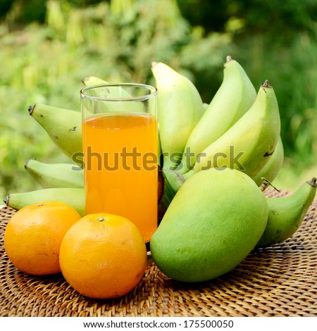 Bananas, mango, oranges and fresh orange juice from organic orchard in closed-up with natural green background.