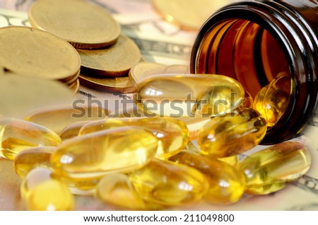Soft gelatin dietary supplement oil capsule and money in drug expense concept.