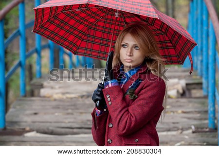 Stylish blonde woman in jacket and gloves standing on bridge and holding umbrella