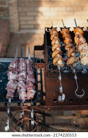Mushrooms strung on skewers and pieces of meat are fried on a forged brazier. To the left of the barbecue are three skewers with raw meat Imagine de stoc © 