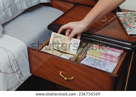 Hand pulls out wad of money from the bedside table filled with Ukrainian cash