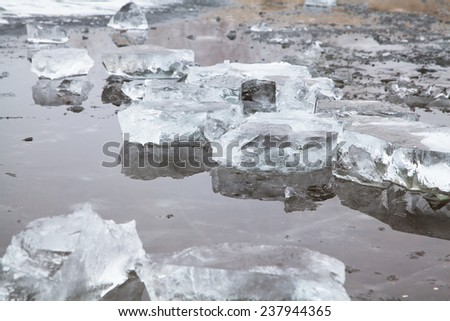 Chunks of ice on a winter frozen river reflected in melt water
