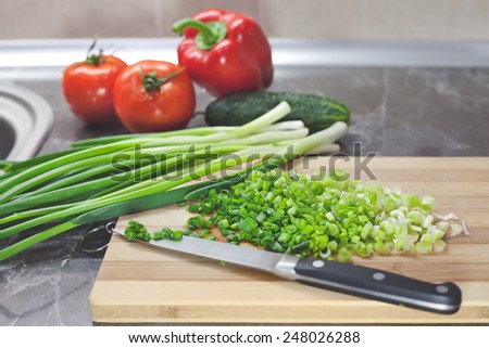 Handful of finely chopped green onions and other vegetables on striped wooden board
