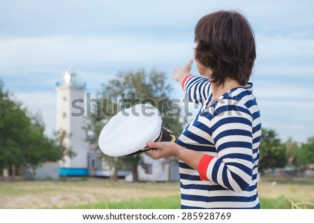 Beautiful elderly woman in a striped dress on the beach at background of old lighthouse