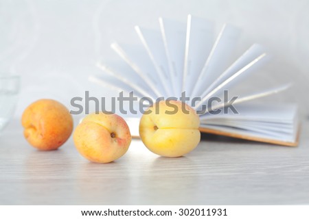 Summer set for reading. Three ripe yellow apricots on a background of open fan pages of the book