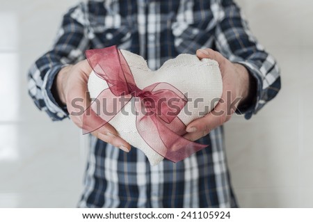 Man in plaid shirt holding a fabric heart with a red ribbon. Valentine's day