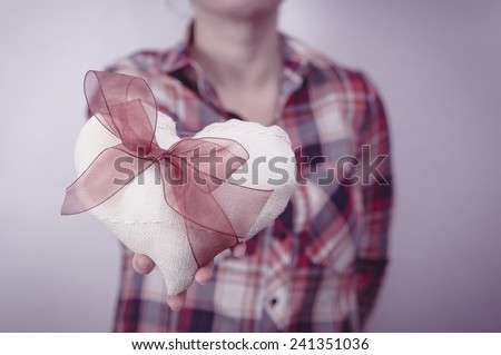 Woman in plaid shirt holding a fabric heart with a red ribbon. Valentine\'s day