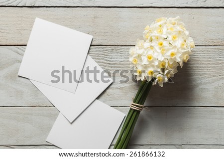 White narcissus flowers and blank paper pieces on wooden background