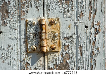 An old rusty door hinge mounted on a paint-flaking door.
