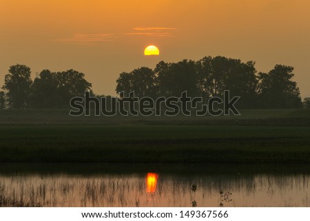Sunrise over a valley. The sun reflects in a small pond.