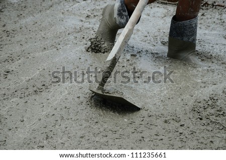 Worker using hoe to smooth wet cement surface.
