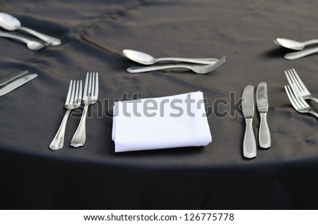 Close up of spoon and fork with white napkin on black table linen.