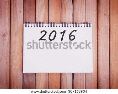 Happy new year 2016 number on white spiral notepad with wood panel background. Vintage style.