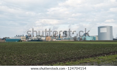 wide angle shot of a sugar mill factory creating smoke in front of a cloudy sky