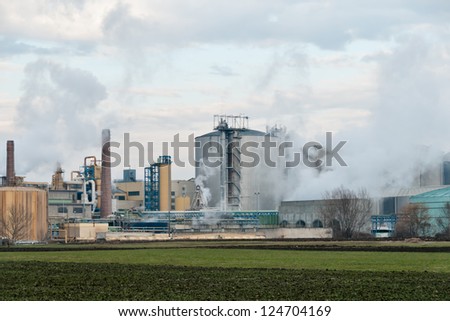 A sugar mill factory creating smoke in front of a cloudy sky