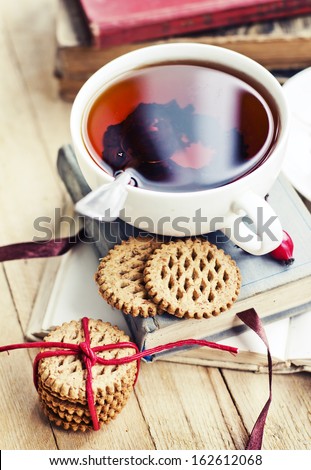 rosehip tea on old books/tea home with books/romantic autumn vintage background with books and tea/cup of tea with hip roses on wooden table/cookies with cup of black tea on wooden background