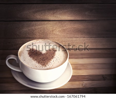 Warm cup of coffee on brown background with heart