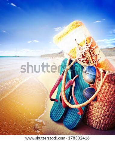 Summer accessories, swimsuit, sun glasses, bag and flip-flops. Closeup of summer beach bag and straw hat on sandy beach.