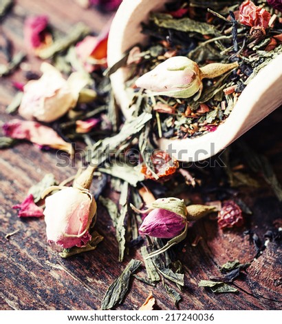 Flower tea rose buds with green dry tea on old wooden table