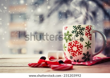 Hot Coffee cup on a frosty winter day window background with candy canes /Christmas holidays background/ Winter cozy background