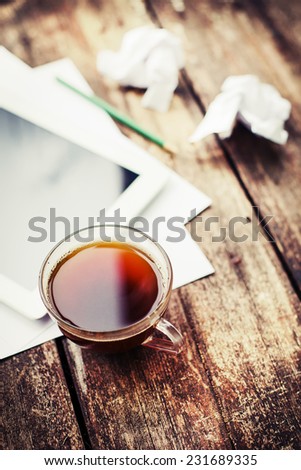 Digital tablet with note paper and cup of tea on old wooden desk. Simple workspace or coffee break in morning/ selective focus