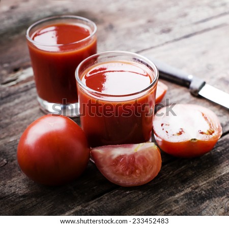 Glasses of tomato juice on wooden table, on wood plants background, fresh drink/ Still-life of fresh tomatoes and juice on a wooden table.