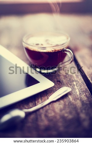 Digital tablet  and cup of coffee on old wooden desk. Simple workspace or coffee break in morning/ selective focus