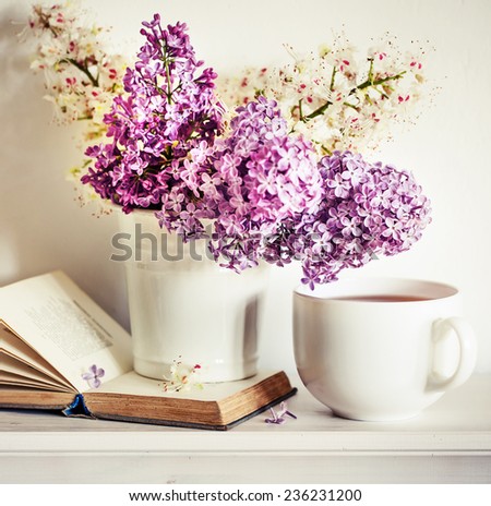 Romantic background with cup of tea ,lilac flowers and open book over white table