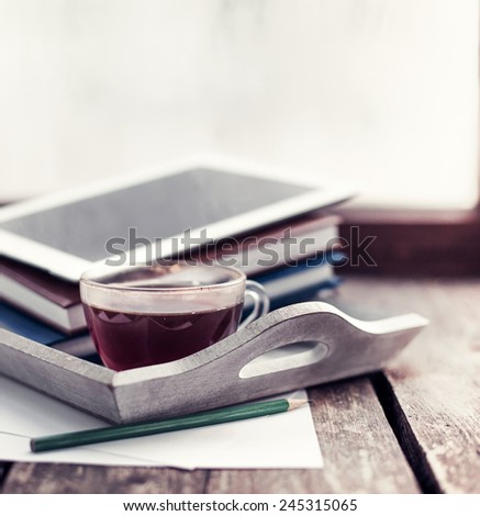 Digital tablet and cup of coffee on old wooden desk. Simple workspace or coffee break in morning/