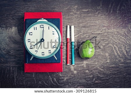 Alarm clock, book stack and felt pens. Schoolchild and student studies accessories. Back to school concept.
