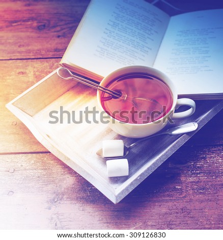 Cup of hot tea and book on a wooden tray