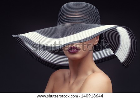 Beautiful young woman wearing summer hat with large brim over dark background