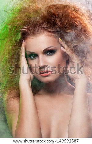 Portrait of beautiful girl in smoke with long red fluffy hair and dramatic makeup