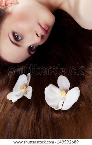 Beautiful girl lying on the floor with two white orchids in her long hair