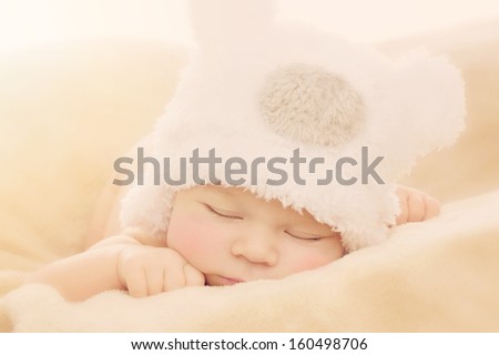 Portrait of newborn baby boy wearing funny bear shape hat sleeping on soft beige cover
