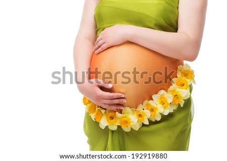 Closeup photo of girl\'s pregnant belly with arms around it and flower decoration over white background