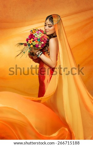 Beautiful young bride wearing orange dress and long veil sniffing wedding bouquet