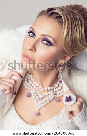 Closeup portrait of beautiful young woman with bright purple make up over snow background