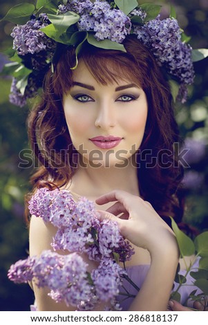 Close-up portrait of beautiful young woman with red hair and lilac on head and in hands. Outdoor shot.