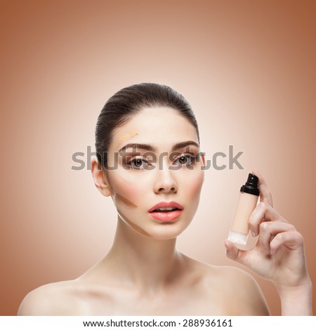 Close-up of beautiful young woman with four shades of liquid foundation on face and bottle in hand. Isolated over brown background. Copy space. Square composition.