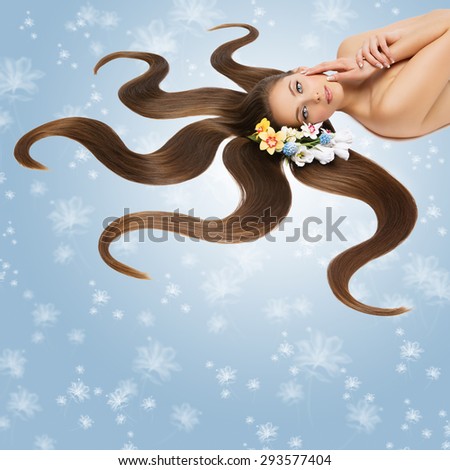 Beautiful young woman with very long natural hair and flowers on it lying on back. Looking into camera. Isolated over blue background with flower bokeh. Square composition.