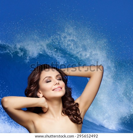 Beautiful young woman with long silky curly hair and makeup. Isolated over splashing wave blue background. Square composition. Copy space.