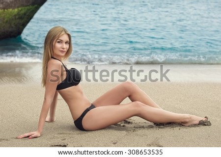 Beautiful young woman in bikini lying on sand near water. Outdoor shot. Tenerife.