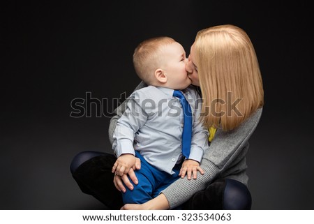 Yong woman kissing child over dark background. Mother and son. Studio shot, Copy space.