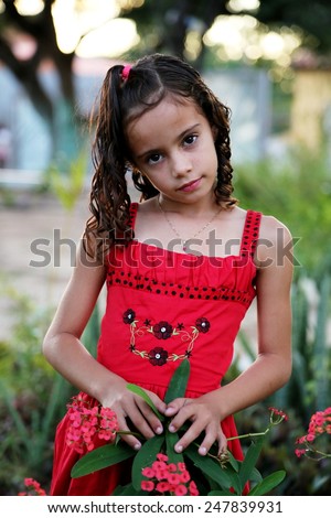 Child with red dress making model pose in the garden