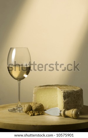 Cutting board with genuine Italian food. White wine glass, ripe hard cheese from ewe's milk and walnuts. Warm ray of light in the background. Space for text