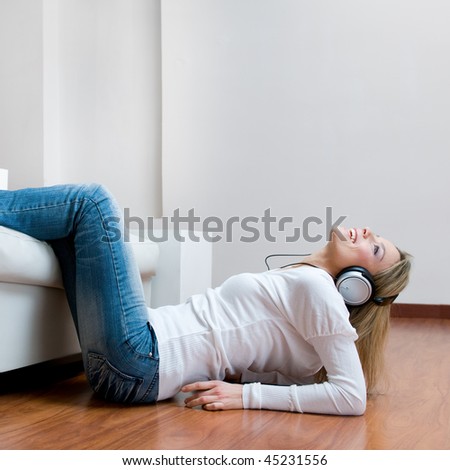 Young girl listening relaxing music with headphones lying on wooden floor