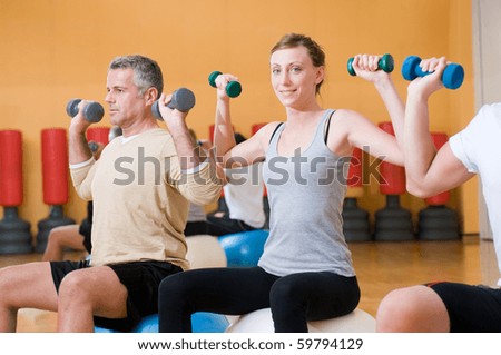 Young lady smiling and looking at camera while lifting weigths on a fitness ball at gym